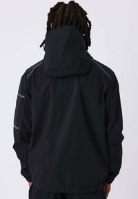 Giacca nera impermeabile con cappuccio, caratterizzata da una texture liscia e dettagli riflettenti sulle spalle e sulle maniche. Polsini e orlo elastici.