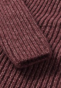 Gros plan sur un tissu tricoté doux et côtelé de couleur rose poudré, montrant des motifs de points verticaux distincts et une texture confortable.
