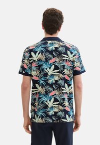 Kortærmet polo t-shirt med en marineblå baggrund og et farverigt tropisk bladmønster i pink, teal og grøn. Blødt stof med krave.