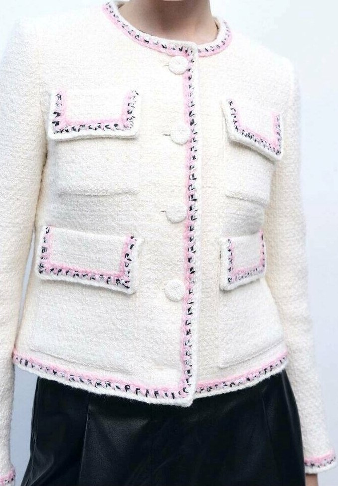 Veste blanche texturée avec bordure rose et noire, dotée de quatre poches à rabat devant et de boutons ronds, portée avec un bas noir.