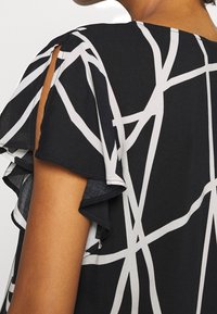 Černá blůza s bílými abstraktními liniemi, krátkými volánovými rukávy a výřezem na ramenou. Lehká tkanina s hladkým povrchem.