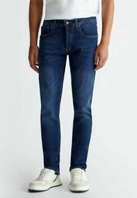 Mörkblå denimjeans med slim fit-design. Har fem fickor, kontrasterande sömmar och en subtil blekt struktur. I kombination med vita sneakers.