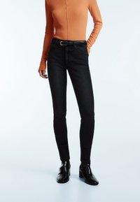 Smarte svarta jeans med hög midja som har en slät textur och ett bälte med silverspänne. Matchat med en åtsittande långärmad topp i orange.