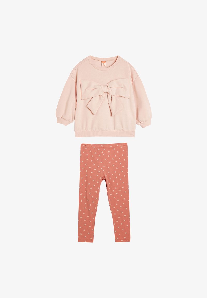 Roze sweatshirt met een grote strik op de voorkant, gecombineerd met roze leggings met kleine witte hartpatronen. Gladde stof, casual ontwerp.