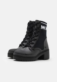 Bottines noires avec une tige en cuir mat et en tissu, à lacets à l'avant, protection en caoutchouc sur les orteils et talon bloc épais. Présentent un revers en tricot avec logo.