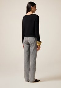 Schwarzer Strickpullover mit langen Ärmeln, kombiniert mit hellgrauen, weiten Jeans. Auffälliges goldfarbenes Armreif und schwarze flache Sandalen.