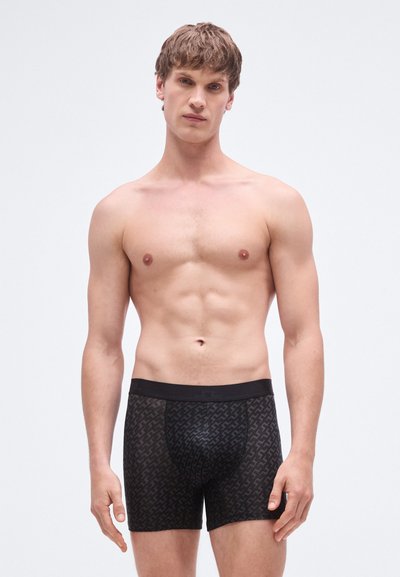 Cuecas boxer pretas com um padrão texturizado. A cintura é preta sólida, enquanto o tecido apresenta um desenho geométrico subtil num tom ligeiramente mais escuro.