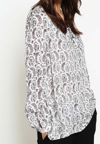 Blusa bianca a maniche lunghe con un motivo paisley nero e rosso, caratterizzata da una vestibilità rilassata, dettagli a bottoni e polsini arricciati.