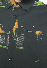 Chemise sombre à boutons avec un imprimé graphique abstrait et coloré comprenant des détails orange, verts et roses, et un logo Volcom sur la poche poitrine.