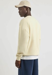 Suéter oversize color crema con textura acanalada, con hombros caídos y diseño sencillo, superpuesto sobre una camisa blanca.