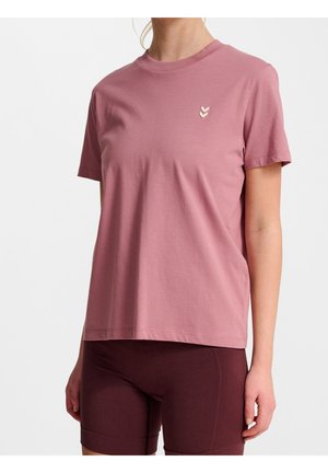 Personne portant un t-shirt mauve uni à manches courtes avec un petit logo chevron blanc sur la poitrine et un cuissard de vélo bordeaux foncé.