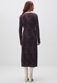 Langärmliges Midi-Kleid in Dunkelpink mit einem strukturierten Zebra-Print. Es hat eine taillierte Taille und einen fließenden Rock, kombiniert mit knielangen weißen Stiefeln.