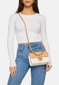 Quilted Handtasche mit einem cremefarbenen Korpus und einem braunen Deckel, ergänzt durch einen goldenen Kettenriemen und einem runden Logodetail auf der Vorderseite.