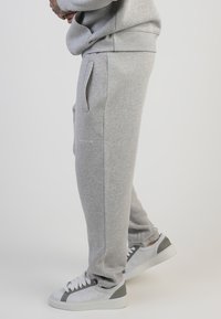 Graue Sweatpants aus weichem Stoff, mit Seiten Taschen und einem Logo-Druck. Kombiniert mit weißen Sneakers mit grauen Akzenten.