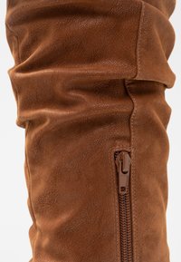 Brown faux leather over-the-knee boot with textured upper, gathered detailing, and a side zipper for closure.