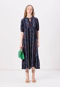 Floral-patterned, navy-blue dress with puffed sleeves, a tie neckline, and tiered hem. Accessorized with a small green handbag.