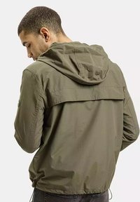 Kapturowa oliwkowa kurtka z lekkiego, teksturowanego materiału. Posiada yoke z tyłu oraz elastyczne mankiety. Minimalistyczny design bez widocznych elementów metalowych.