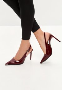 Burgundin värinen patentoitu nahka slingback-korkokengät, joissa on teräväkärkinen malli, korkea stiletto-korko ja hopeanvärinen yksityiskohta korkojen kohdalla.