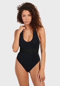 Crni jednodijelni kupaći kostim s dubokim izrezom i teksturiranim crnim pojasom. Glatki materijal; visoko izrezane nogavice.