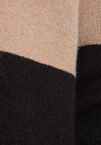Knit sweater fabric featuring beige and black color blocks, with a soft texture and a smooth finish. Contains no visible patterns or hardware.