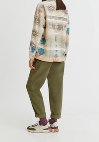 Pull à motif tricoté avec des tons terreux, pantalon vert olive et baskets légères avec des accents violets. Bords de manches retroussés et chaussettes texturées.