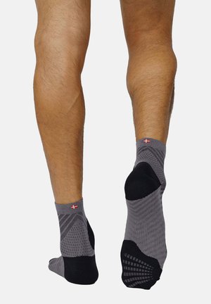 Graue Sportsocken mit einem strukturierten Muster, schwarzen Akzenten an Ferse und Zehen sowie einem kleinen rot-weißen Logo am Bund.