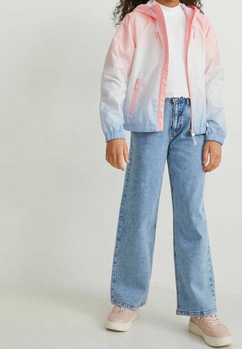 Let jakke i pink til blå gradient med elastiske manchetter, lynlåslommer og snoretræk på hætten, parret med højtaljede blå jeans og pastelfarvede sneakers.