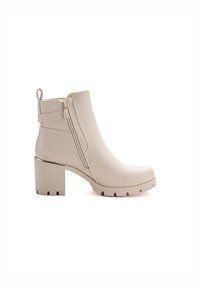 Botas de tobillo beige hechas de cuero sintético, con un alto tacón bloque, cremalleras laterales y suela de goma texturizada con agarre.