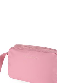 Bolso de hombro de tela suave en color rosa con cierre de cremallera. Presenta el logotipo en relieve "SKECHERS" en la parte frontal y una correa ajustable.