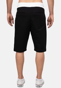 Shorts noirs avec une taille élastique blanche, dotés de deux poches arrière et d'une coupe à longueur de genou. Texture lisse et design décontracté.