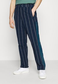 Navy striped pants with vertical lines, featuring a teal accent on the side. Made of soft fabric, loose fit with side pockets.