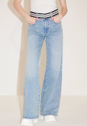 Jeans a zampa d'elefante di un azzurro chiaro con vita alta, dotati di una cintura a righe bianca e nera. Il tessuto è di denim con una texture liscia.