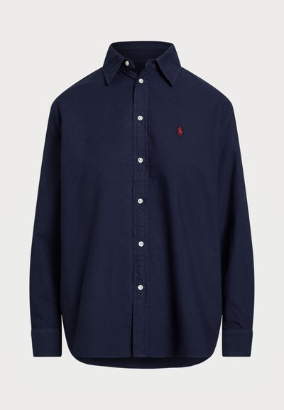 Ναυτικό μπλε μακρυμάνικο πουκάμισο με κουμπιά από βαμβάκι. Διαθέτει κλασικό γιακά, κουμπωτό μπροστινό μέρος και ένα μικρό κόκκινο λογότυπο στο αριστερό στήθος.