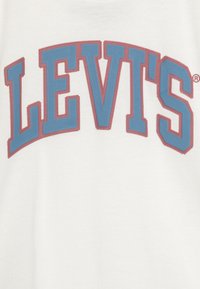 Camiseta blanca de algodón con un gran logo de Levi's en rojo y azul en un diseño de arco redondeado con letras texturizadas.