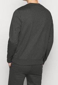 Sudadera gris oscuro de manga larga, con cuello redondo, puños y dobladillo acanalados, hecha de una suave tela texturizada y con un corte relajado.