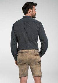 Mannen donker gestreepte lange mouwen shirt met een kraag, gecombineerd met lichtbruine leren shorts met decoratieve stiksels en een riem.