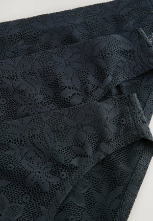 Tissu en dentelle marine avec des motifs floraux, présentant des découpes intricantes. Le matériau a une apparence texturée et une qualité légèrement transparente.