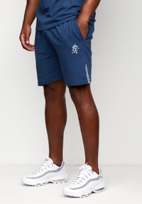 Shorts de sport navy avec poches latérales, taille élastique et accents gris. Portés avec des baskets blanches à détails gris et à design texturé.
