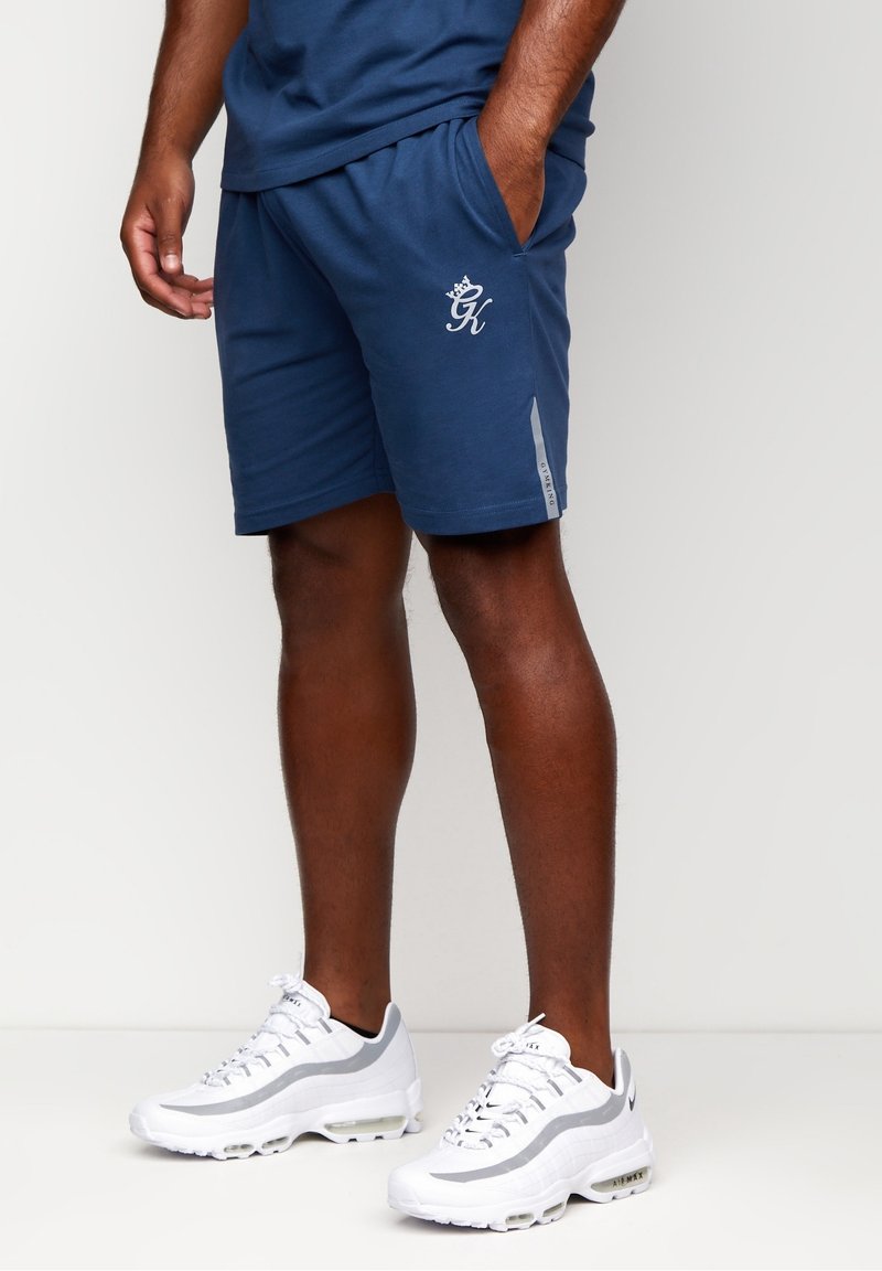 Shorts de sport navy avec poches latérales, taille élastique et accents gris. Portés avec des baskets blanches à détails gris et à design texturé.