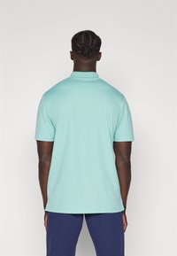 Polo skjorte i lys teal, korte ermer, laget av glatt stoff, har klassisk krage og rett kant, vist fra ryggen.