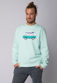 Sweatshirt vert menthe arborant un graphique d'un van de camping vintage avec une planche de surf sur le toit. Fabriqué dans un tissu doux avec des poignets côtelés.