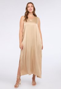 V-kaula beige satiinimekko, jossa on hihaton muotoilu ja sivuhalkiot liikkumisen helpottamiseksi. Pehmeä rakenne ja lentävä siluetti.