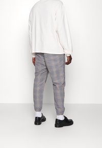 White long-sleeve shirt paired with gray checkered pants featuring orange accents and elastic cuffs, complemented by black shoes and white socks.