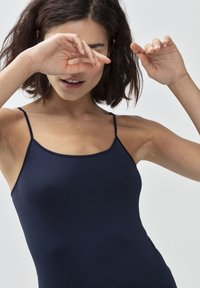 Granatowy dopasowany top na ramiączkach z cienkimi paskami, wykonany z gładkiego, elastycznego materiału. Charakteryzuje się prostym, klasycznym wzornictwem bez wzorów czy ozdób.