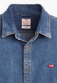 Camicia in denim slim-fit di colore blu scuro. Presenta colletto classico, chiusura a bottoni e una piccola etichetta rossa con il logo Levi's sul lato sinistro del petto.