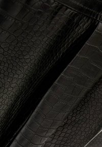 Czarna sztuczna skóra o fakturze wzoru reptilia. Charakteryzuje się różnorodnymi łuskami i gładkimi partiami, podkreślając nowoczesny design.