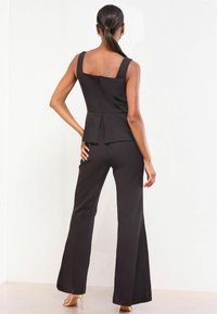 Čierny peplum top so štvorcovým výstrihom, skombinovaný s čiernymi rozšírenými nohavicami. Hladká látka, viditeľný zips na chrbte, obuté s béžovými podpätkami.
