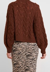 Brown cable-knit sweater with a high neck and voluminous sleeves, paired with a beige skirt featuring a black zebra print pattern.