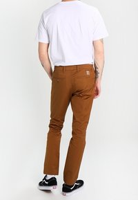 Bruine broek van geweven stof, met een slim fit, achterzakken en een logo patch. Gecombineerd met een eenvoudig wit t-shirt en zwarte sneakers.