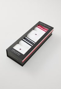 Vier Paare weißer Socken in einem Geschenkpakt, mit roten und marineblauen gestreiften Akzenten sowie einem Logo. Die Box hat ein schwarzes, elegantes Design.